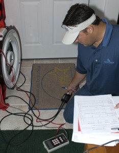 Photo of research knelt down adjusting controller of blower door for energy audit.