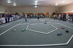 Remote controlled, model-sized hydrogen fuel cell cars race on carpeted track with PVC barriers.