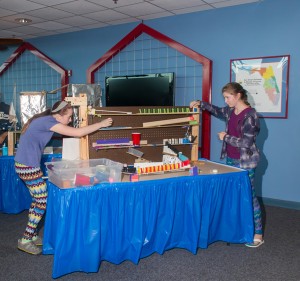 Two girls standing on either end of six foot table, setting up hydrogen challenge contraption.
