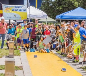 Two students race their model-sized solar cars while a crowd looks on.