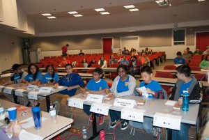 Two, four-member teams sit at tables, each having a buzzer in front of them.