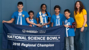 Winning students and teacher standing in front of banner, wearing ribbons and holding trophy.