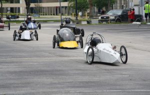 Six electrathon cars shown racing on parking lot track.