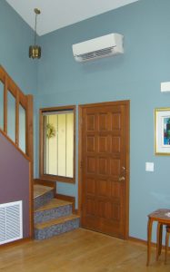 Interior of townhouse with staircase by front door. Return air grill under on side of staircase with mini-split ac unti above front door.