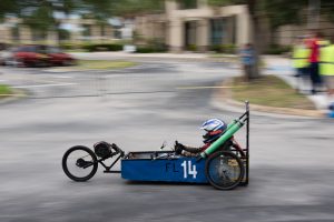 Blue electric go-cart number 14 racing, blurred background.