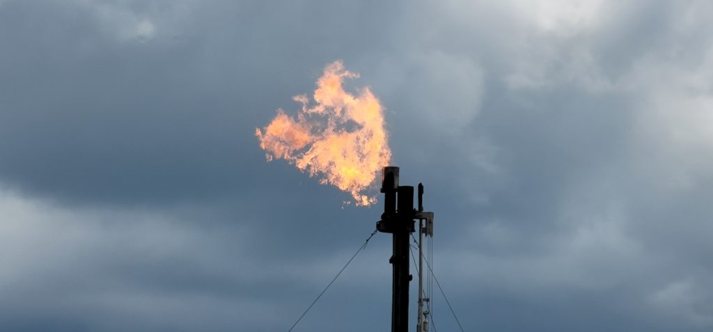 Closeup of gas burning from well head with clouds in background