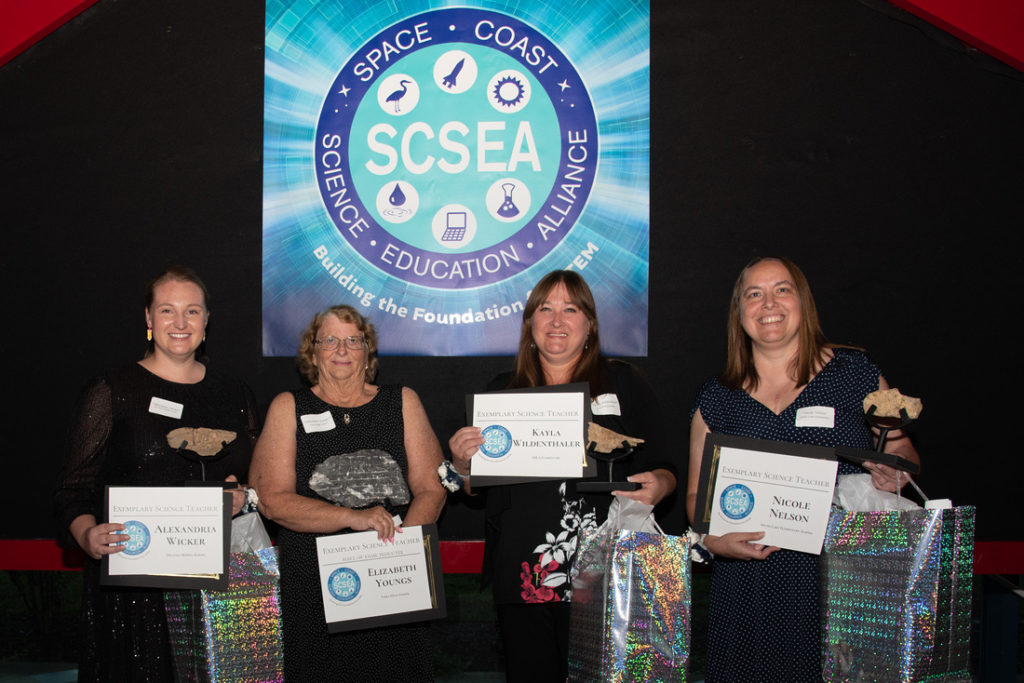 Photo of award winners holding their gifts in front of sign.